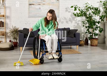 Eine junge Frau im Rollstuhl fegt den Boden ihres Wohnzimmers. Sie lächelt und blickt auf den Besen. Stockfoto