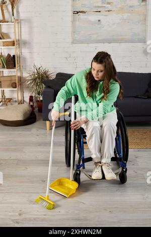 Eine junge Frau im Rollstuhl fegt mit einem Besen und einer Kehrschüssel den Boden ihres Wohnzimmers. Stockfoto