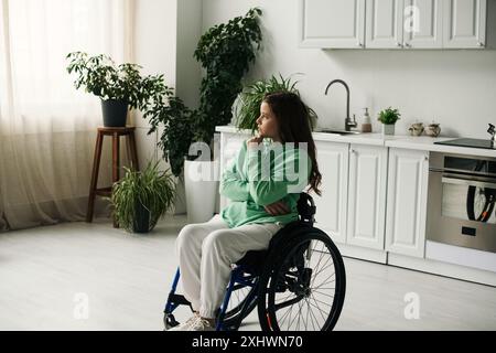 Eine junge Frau im Rollstuhl sitzt in ihrem Wohnzimmer, verloren in Gedanken. Stockfoto