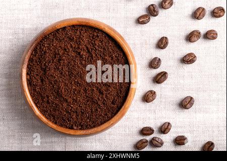 Kaffeepulver, frisch gemahlene Kaffeebohnen in einer Holzschale auf Leinengewebe. Rechts geröstete Samen von Beeren aus Coffea arabica. Stockfoto