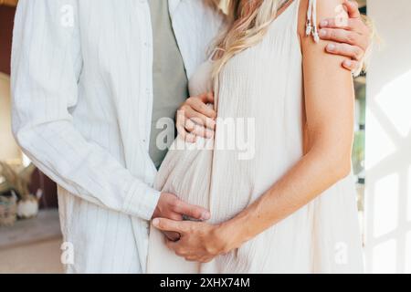 Abgeschnittenes Bild einer schwangeren Frau und ihres Mannes, die den Bauch umarmen Stockfoto