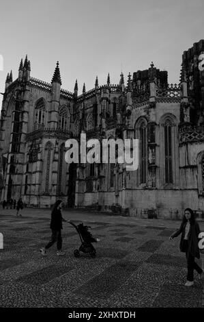 Besucher schlendern vor dem batalha-Kloster mit seiner komplizierten gotischen Architektur als Kulisse unter einem ruhigen Abendhimmel Stockfoto