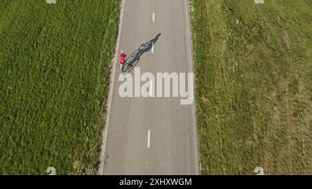 Weibliche Rennradfahrerin, die auf einer leeren, flachen Asphaltstraße in die Pedale tritt, an einem sonnigen Sommertag, Luftdrohnen-Tracking-Aufnahme. Stockfoto