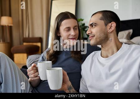 Ein junges schwules Paar genießt einen entspannenden Morgen in ihrem Schlafzimmer und teilt einen gemütlichen Moment mit einer Tasse Kaffee. Stockfoto