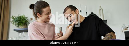 Ein junges schwules Paar genießt einen gemütlichen Moment zusammen in ihrem modernen Zuhause, wo es lacht und einen Happen zu essen gibt. Stockfoto