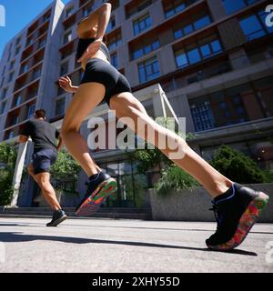 Dynamische Tiefwinkelaufnahme von zwei Läufern in einer Stadt, die sich auf die farbenfrohen Turnschuhe und die muskulösen Beine der Frau konzentriert. Stockfoto