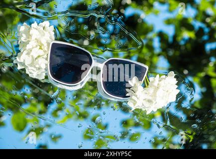 Schwimmende Sonnenbrille mit floralen Akzenten auf abstraktem Hintergrund. Stockfoto