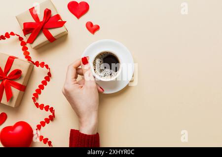 Flache Lage einer herzförmigen Tasse schwarzen Kaffees in den Händen von Frauen auf farbigem Hintergrund mit Kopierbereich Draufsicht. Valentinstag- und Feiertagskonzept. Stockfoto