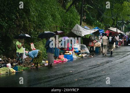 Regnerische Straßenmarktszene mit Leuten, die Regenschirme und Einkaufstaschen auf einer nassen Straße in Ella, Sri Lanka, tragen. Stockfoto