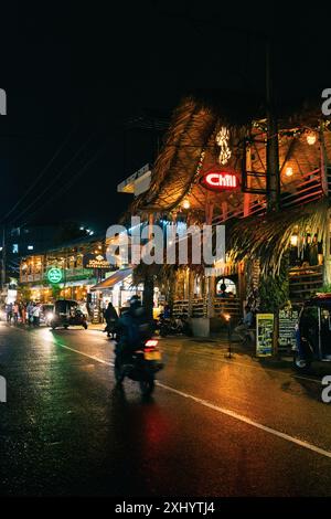 Nachtszene einer lebhaften Straße mit farbenfrohen Neonlichtern und Menschen, die an belebten Restaurants und Cafés vorbeischlendern Stockfoto