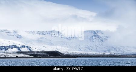 Nördliche Küstenlandschaft mit schneebedeckten Bergen unter dramatischem blauen Himmel. Reykjavik und Umgebung, Island. Panoramafoto mit blauem Farbkorrekturfilter ef Stockfoto