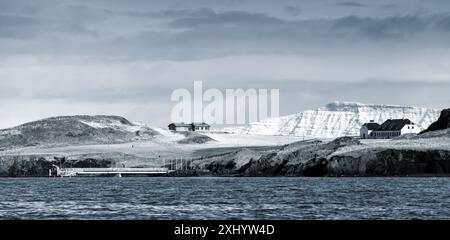 Reykjavik und Umgebung, Island. Nördliche Küstenlandschaft mit schneebedeckten Bergen unter dramatischem blauen Himmel. Panoramafoto mit verblassten Farben und blauem Dekor Stockfoto