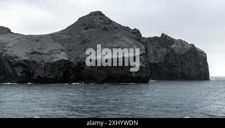 Felsige Küsten der Insel Vestmannaeyjar. Natürliche dunkle Landschaft Islands, blauer Panoramahintergrund Stockfoto