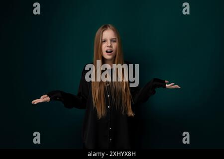 Eine Frau mit leuchtend langen roten Haaren steht selbstbewusst vor einem grünen Hintergrund. Ihr Haar fließt über den Rücken, während sie nach vorne blickt. Stockfoto