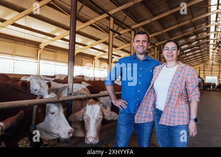 Ein junges Ehepaar in einem Kuhstall. Eine lächelnde Frau und ein junger Mann lachen und umarmen sich in einer Scheune auf einer Farm. Ein glücklicher Ehemann und eine glückliche Frau in zwangloser Atmosphäre Stockfoto