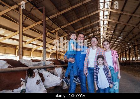 Eine glückliche Bauernfamilie in einem Kuhstall. Ein junges verheiratetes Paar und ihre Kinder kümmern sich um Haustiere auf dem Bauernhof. Eine lächelnde Mutter und eine kleine Tochter Stockfoto