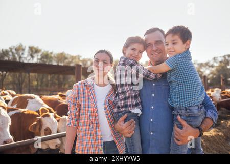 Eine junge glückliche Familie von Bauern in einem Kuhstall. Eine lächelnde Frau, ein Mann und zwei Kinder in lässiger Kleidung kümmern sich um die Haustiere auf der Farm. Mom und Dad Witz Stockfoto