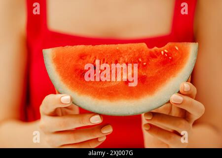 Nahaufnahme gepflegter weiblicher Hände mit einer Scheibe saftiger Wassermelone. Ein Mädchen in einem roten T-Shirt hält ein Stück Wassermelone. Sommerernte. Stockfoto