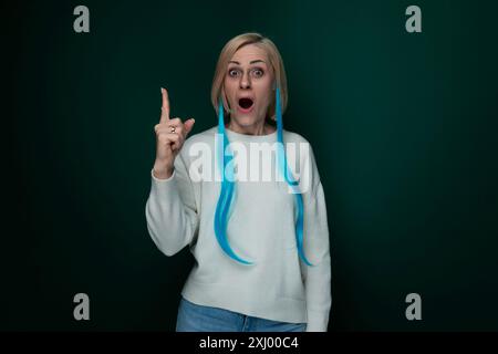 Eine Frau mit leuchtend blauem Haar verzieht ihr Gesicht in einem komischen Ausdruck und zeigt ein verspieltes und humorvolles Verhalten. Ihre Augen werden weiter, der Mund dreht sich, und Stockfoto