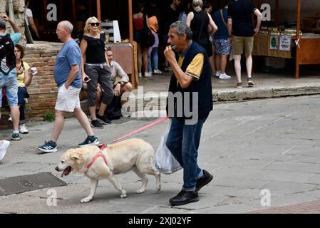 Ein Mann spielt Mundharmonika, während er mit seinem Hund in San Gimignano in der Toskana, Italien, spaziert Stockfoto