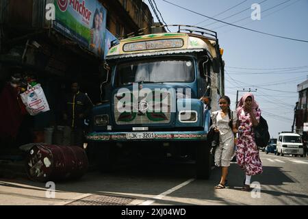 Zwei Sri-lankische Mädchen gehen an einem bunten Vintage-Truck vorbei, der auf einer belebten Straße in Haputale, Sri Lanka, geparkt ist. Stockfoto