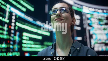 Nahaufnahme Porträt einer jungen Frau mit Brille, die auf große digitale Bildschirme schaut, während Codezeilen angezeigt werden. Professioneller Hacker Durchbricht Das Cybersicherheitsschutzsystem Und Ändert Den Code Stockfoto