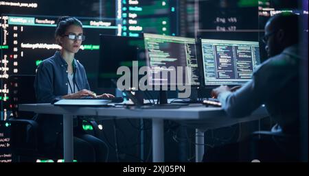Verschiedene junge Männer und Frauen, die an Desktop-Computern arbeiten, umgeben von großen Bildschirmen, die Code Prompts anzeigen. Professionelle Computeringenieure entwickeln autonomen Algorithmus für generative KI. Stockfoto