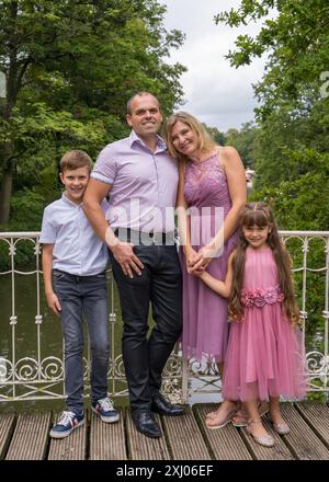 Porträt einer glücklichen Familie. Lachende Papa und Mom, Teenager-Sohn und kleine Tochter stehen auf einer weißen Brücke im Park. Mom und Mädchen sind in bea gekleidet Stockfoto