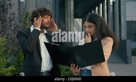 Zwei Geschäftsleute in der Stadt traurig aufgebracht schuldig schuldig arabische Frau Geschäftsfrau Managerin Praktikantin hält Aktenpapiere Dokumente schlechte Ergebnisse Fehler gestresst Stockfoto