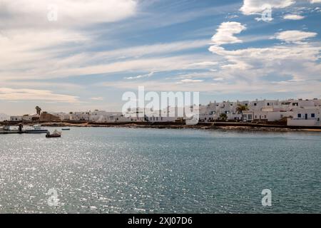 Blick auf die Insel La Graciosa von einem Boot aus. Ruhiges Wasser des Atlantischen Ozeans und eine typische weiße Architektur. Blauer Himmel mit weißen Wolken im Winter. C Stockfoto