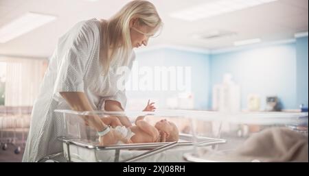 Mutter, die ein neugeborenes Kind auf einem Krankenhausbett in einer modernen Kinderklinik niederlegt. Die Mutter Tröstet Ihr Neugeborenes Kind. Gesundheit, Schwangerschaft und Mutterschaft Konzept Stockfoto