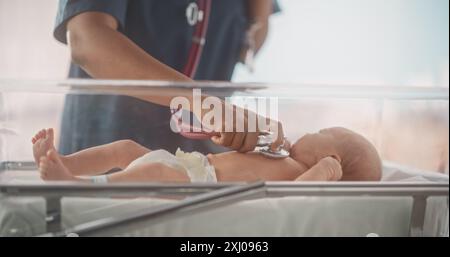 Happy Professional Nurse versorgt ein geborgenes Frühgeborenes auf der Neugeborenen-Intensivstation rund um die Uhr. Afrikanische Ärztin untersucht ein Kind mit Stethoskop in der Kinderklinik Stockfoto