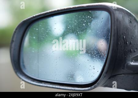 Auto-Seitenspiegel mit Regentropfen auf verschwommenem Hintergrund, Nahaufnahme Stockfoto