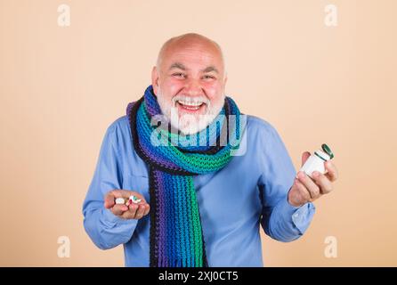 Lächelnder bärtiger Mann mit Medikamentenpillen, täglichen Vitaminen und Nahrungsergänzungsmitteln. Medizin, Behandlungen und Gesundheitswesen. Senior-Mann, mit Schal eingewickelt Stockfoto