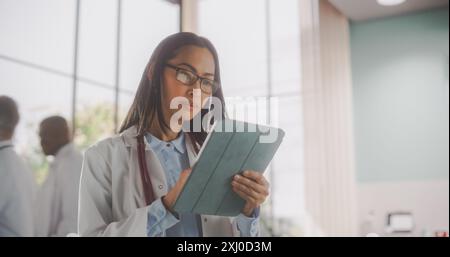 Junge asiatische Ärztin im Weißen Mantel gehen und einen Tablet-Computer im Krankenhaus benutzen. Schöne Weibliche Medizinische Gesundheitspflege Professional Appointing Verschreibungen Online Stockfoto