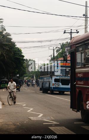 Eine Straßenszene in Mirissa, Sri Lanka, mit Bussen und einem Radfahrer. Die Atmosphäre ist voll, der Verkehr und die Menschen bewegen sich entlang der Straße. Stockfoto