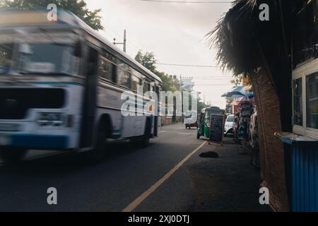 Eine Straßenszene bei Tageslicht in Mirissa, Sri Lanka, mit einem alten Bus, der schnell eine Straße entlang fährt, die von Geschäften und Schildern gesäumt ist. Stockfoto