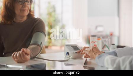Ärztin mit Sphygmomanometer zur Blutdruckmessung bei einer Seniorin in der Gesundheitsklinik. Krankenschwester Bei Älteren Patienten Stockfoto