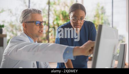 Medizinisches Krankenhaus: Zwei verschiedene Ärzte sprechen und verwenden Computer, diskutieren Testergebnisse, untersuchen Röntgenaufnahmen. Schwarze Chirurgin plaudert mit männlicher Physik Stockfoto