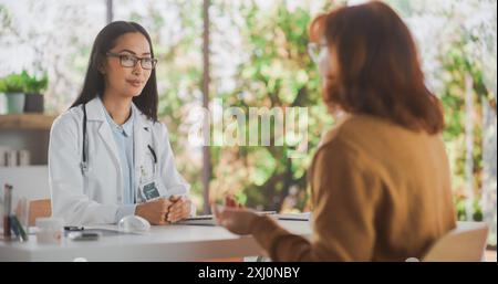 Asiatische Gesundheitsfachkraft, die einem älteren weiblichen Patienten zuhört, bevor sie eine Behandlung für ihren medizinischen Zustand während einer Konsultation in einer Gesundheitsklinik verschreibt Stockfoto