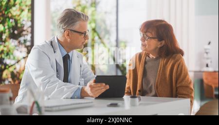 Arzt mittleren Alters, der während der Konsultation in der Gesundheitsklinik mit einer älteren Frau spricht und ihre CT-Scans auf einem Tablet-Computer zeigt. Arzt in White Coat schlägt Behandlung für ältere Patienten vor Stockfoto