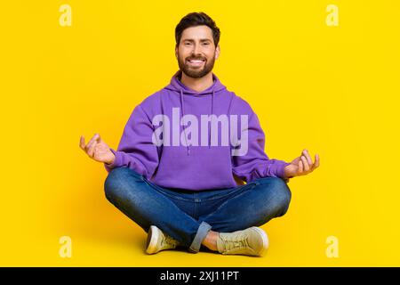 Ganzkörperfoto des attraktiven jungen Mannes sitzen Boden meditieren gekleidete stilvolle violette Kleidung isoliert auf gelbem Hintergrund Stockfoto