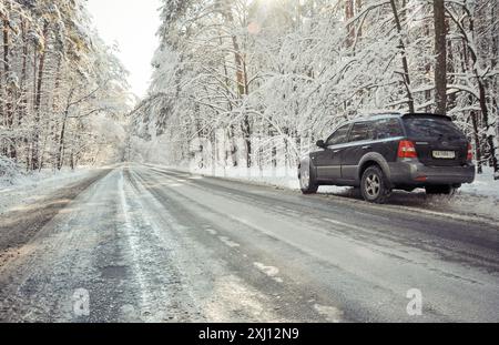 Winterstraße. Weitwinkelbild einer Straße durch einen Winterwald an einem sonnigen Tag. Der schwarze SUV hielt an einer Straßenseite an. Stockfoto