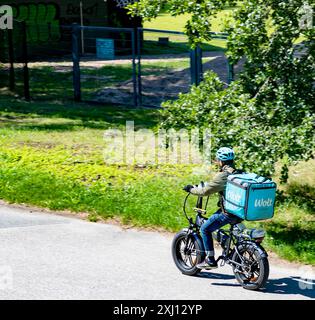 Wolt Kurier auf einem Elektrofahrrad in Mustapuronpolku, Myllypuro, Helsinki, Finnland, im Juli 2024. Stockfoto
