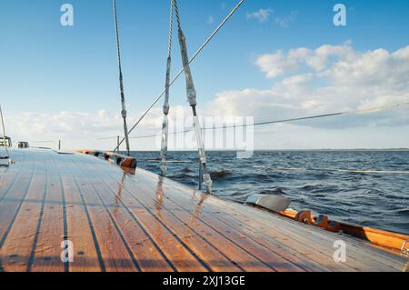 Segeln in einem Meer bei sonnigem Wetter. Himmel teilweise bedeckt mit Wolken, kleine Wellen auf der Oberfläche. Glänzendes hölzernes Yachtdeck bedeckt mit Wassertropfen. Stockfoto