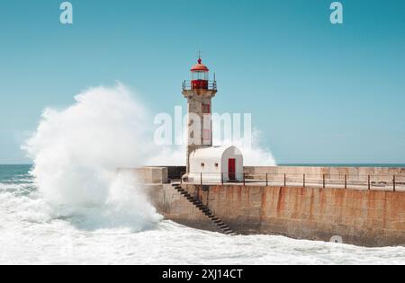 Die Welle stürzt in den Leuchtturm auf dem Steinmole. Der Leuchtturm von Felgueiras an der Mündung des Flusses Douro in Foz do Douro bei Porto. Blauer Himmel und Ozean. Stockfoto