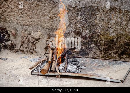 Eine kleine Feuerstelle im Freien leuchtet hell mit Baumstämmen und Anzündungen, die an einer rustikalen Steinmauer platziert ist Stockfoto