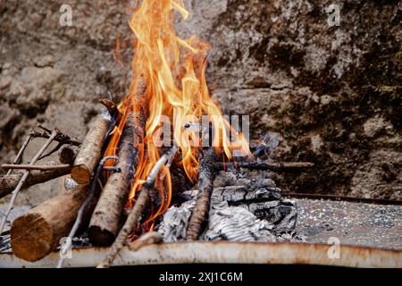 Eine kleine Feuerstelle im Freien leuchtet hell mit Baumstämmen und Anzündungen, die an einer rustikalen Steinmauer platziert ist Stockfoto