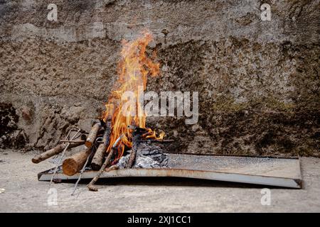 Eine kleine Feuerstelle im Freien leuchtet hell mit Baumstämmen und Anzündungen, die an einer rustikalen Steinmauer platziert ist Stockfoto