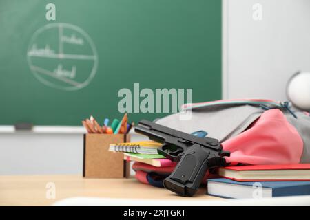 Schulpapier, Waffe und Rucksack auf dem Schreibtisch im Klassenzimmer Stockfoto